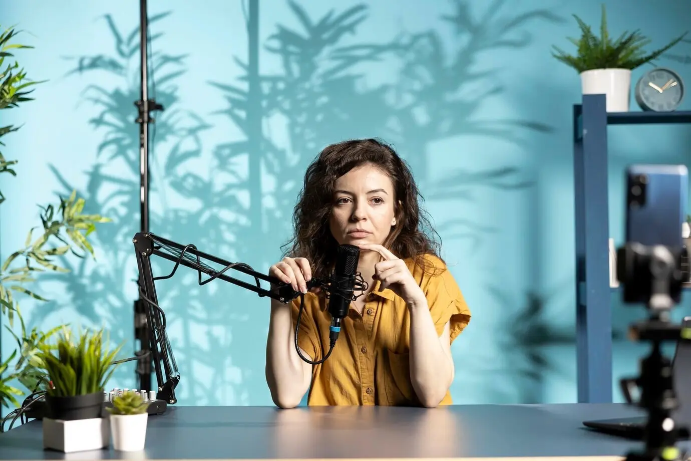 Стример записывает прямой эфир в студии, используя смартфон на штативе и микрофон.